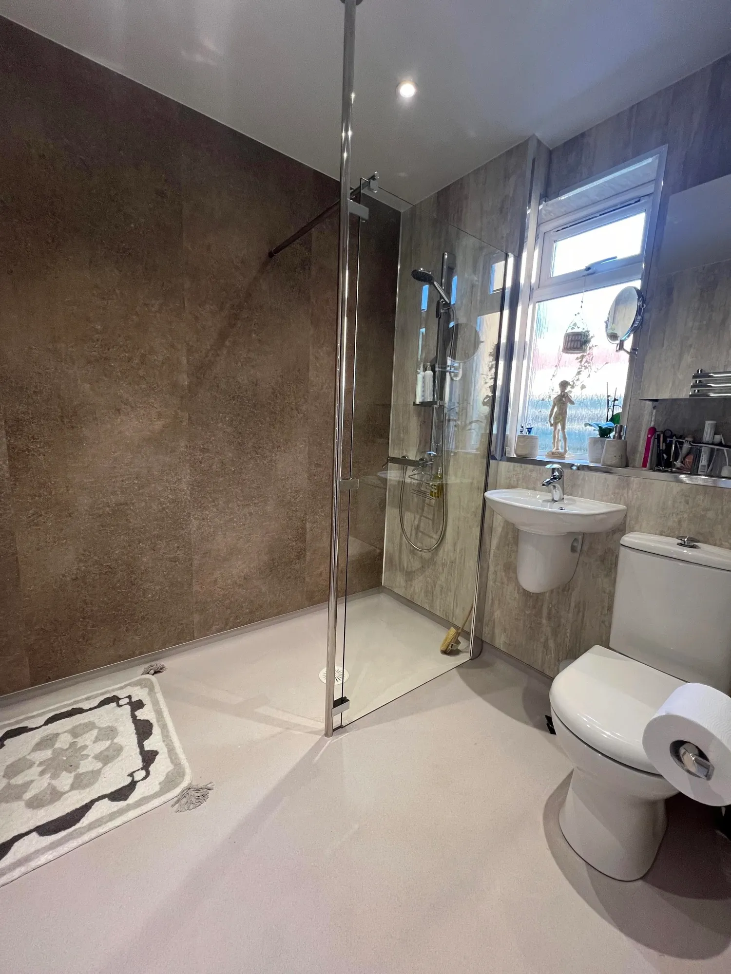 Level-access wet room with grey stone-effect panels and a glass screen