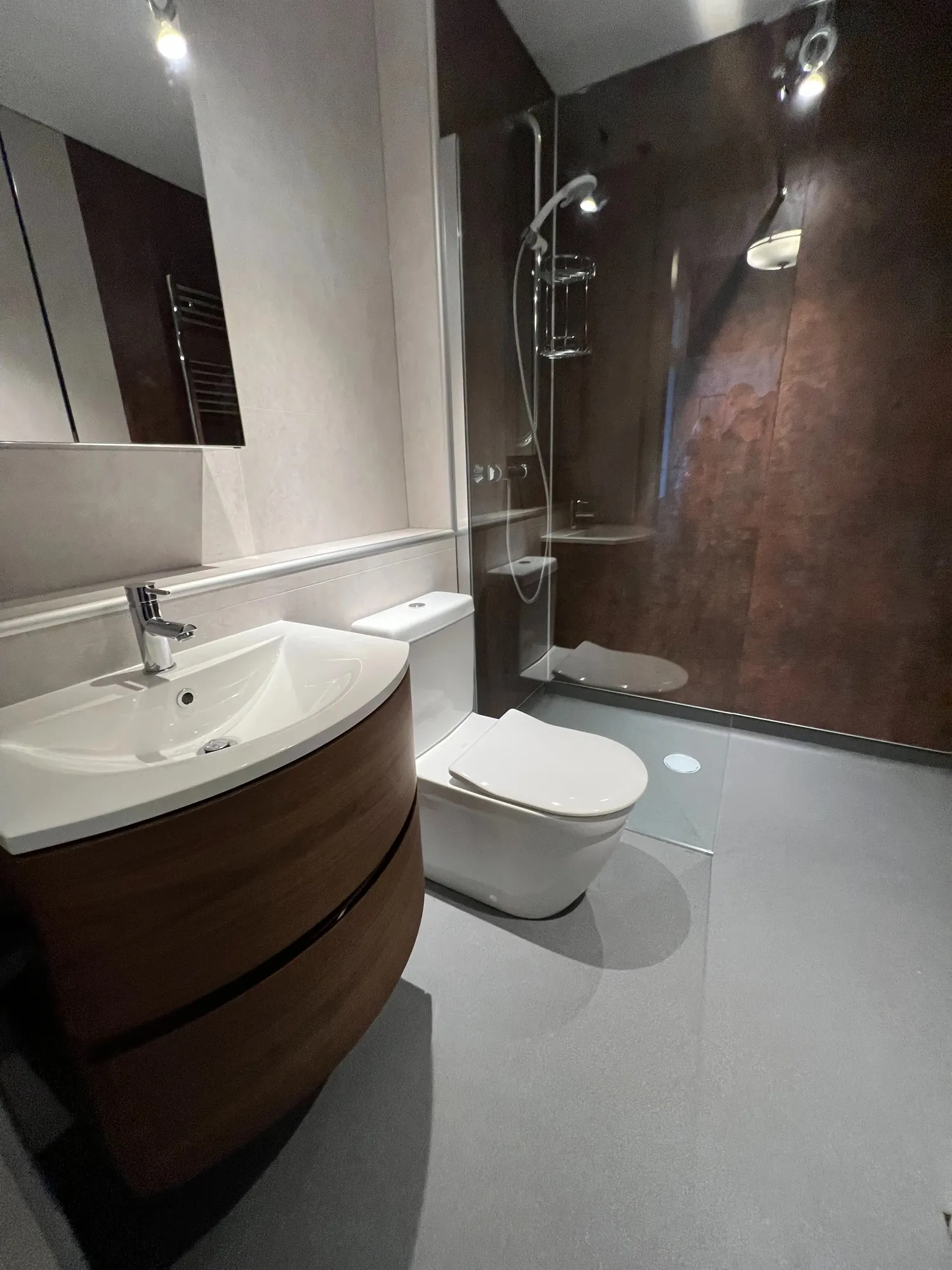 Wet room with dark stone-effect walls and a curved walnut vanity unit
