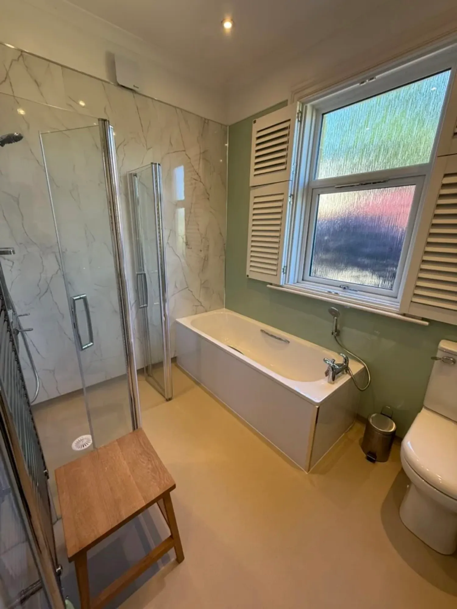 Bath with a glass shower screen and wooden stool