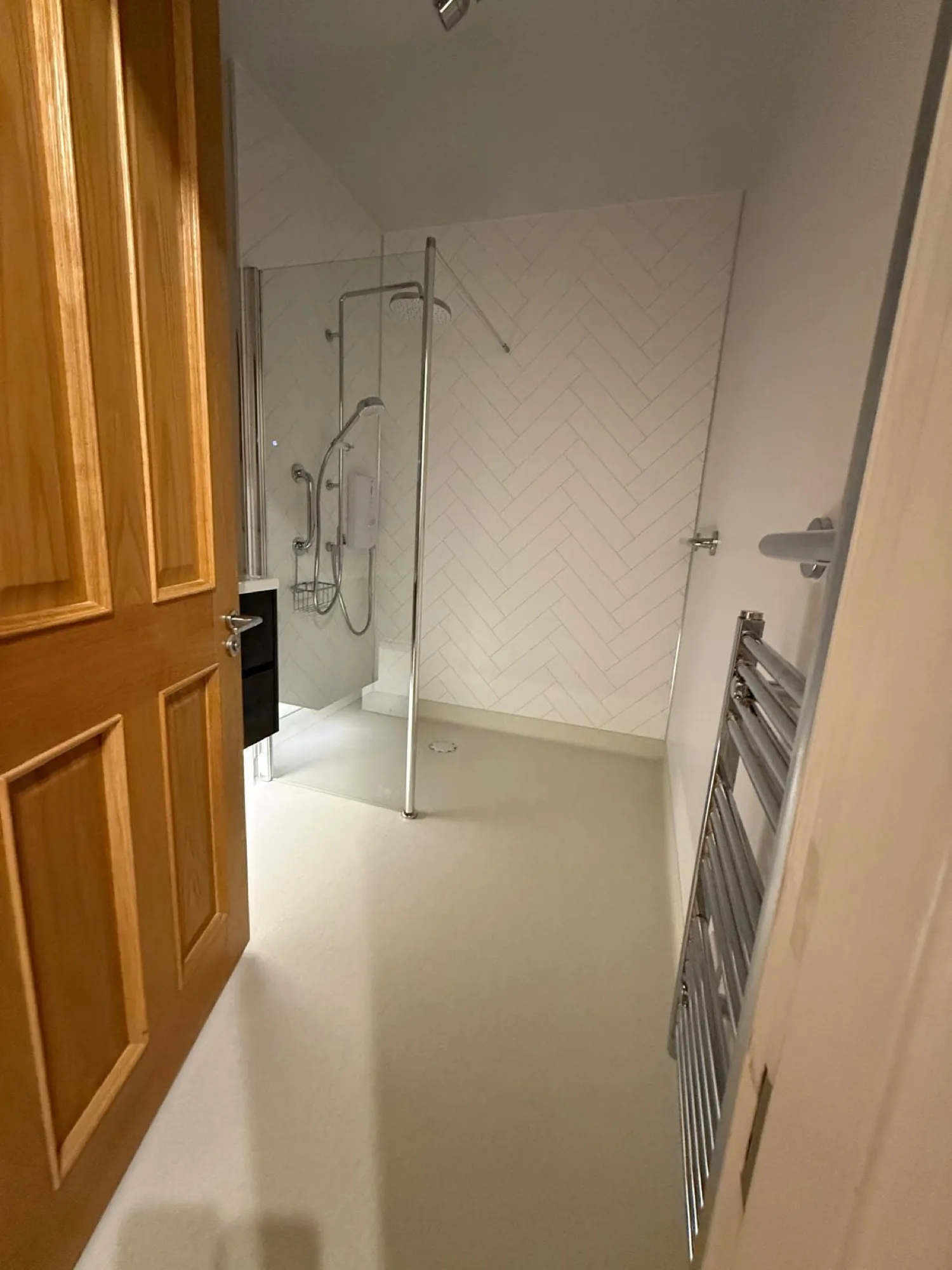 Walk-in shower with a glass screen beside an oak door