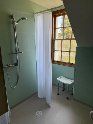 A completed walk-in shower with a folding seat and support rail