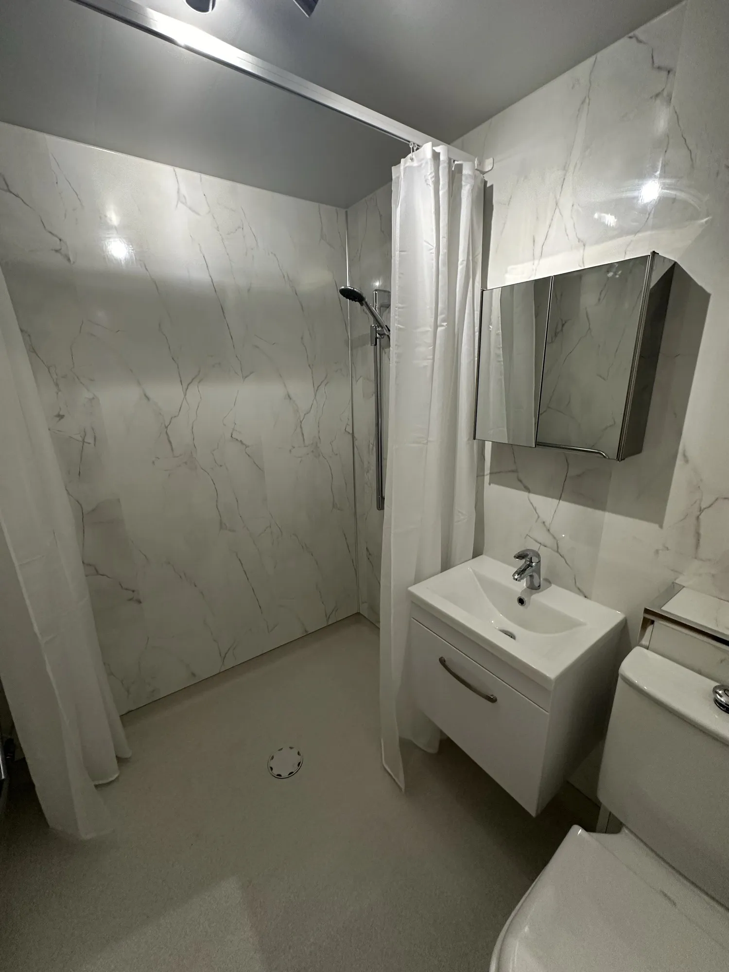 Walk-in shower with white marble-effect panels and a vanity basin