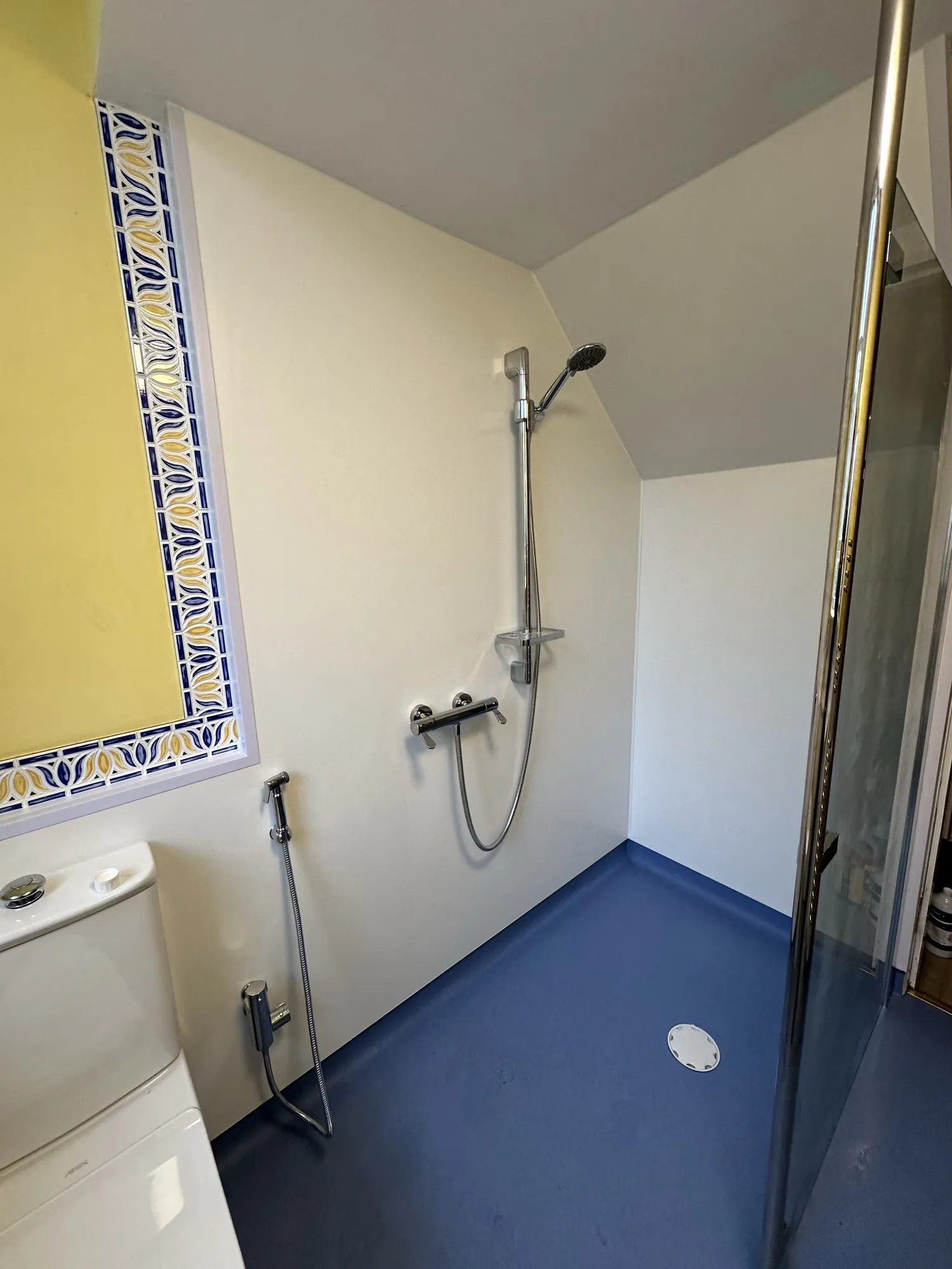 Bathroom with yellow walls, blue safety flooring and a patterned tile border