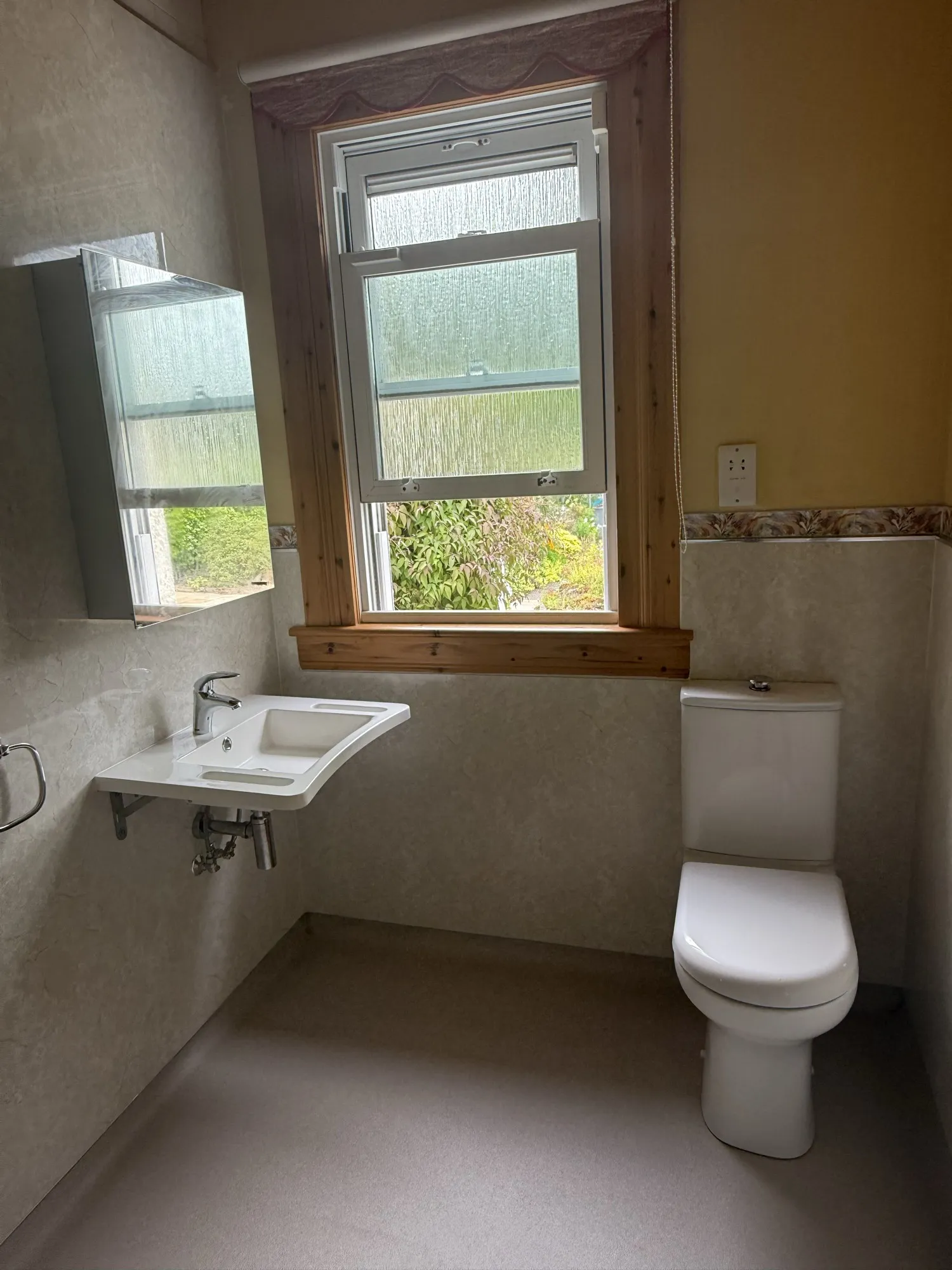 Basin and toilet beneath a timber-framed window