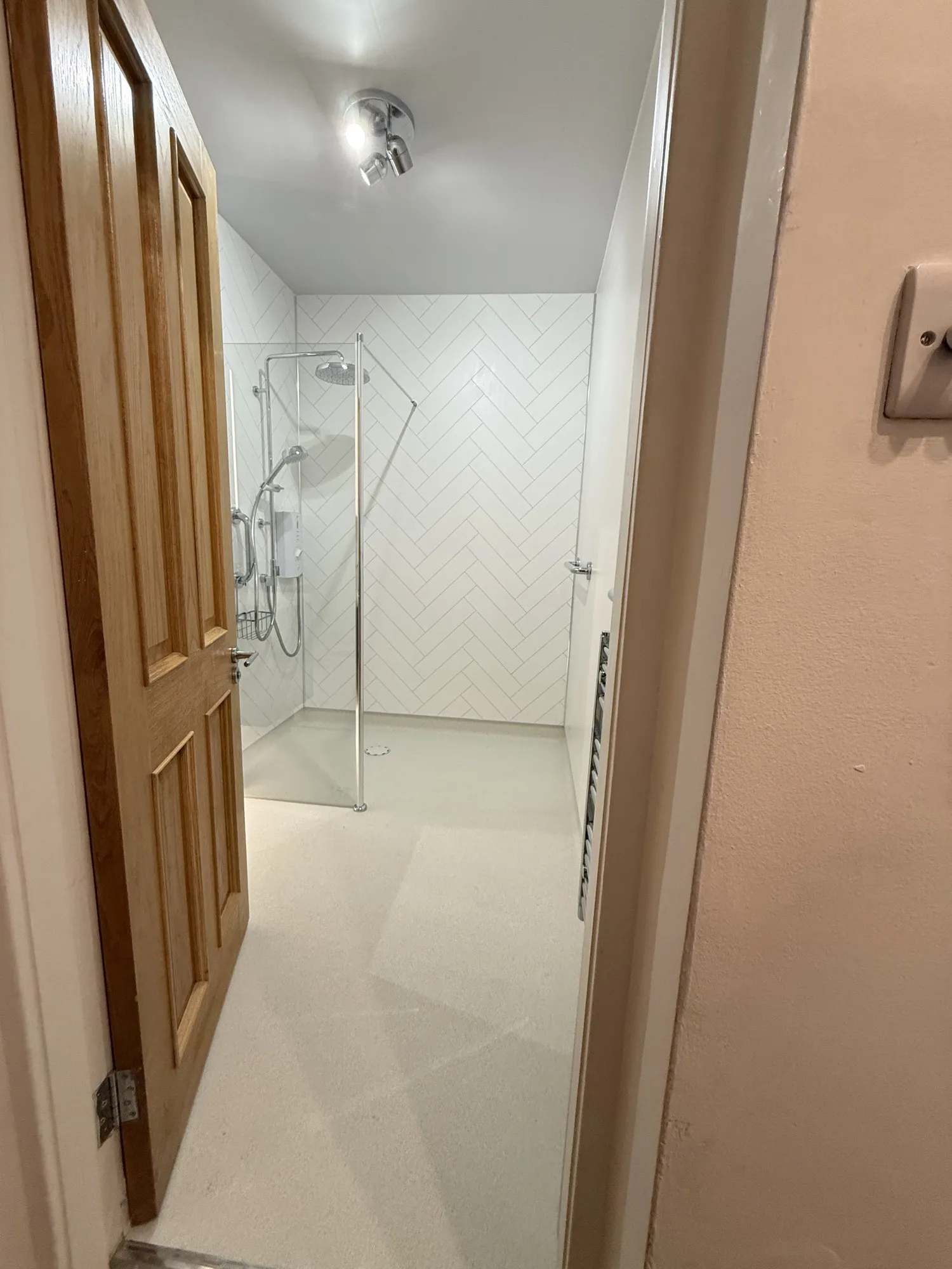 Walk-in shower with herringbone-effect panels seen from the hallway