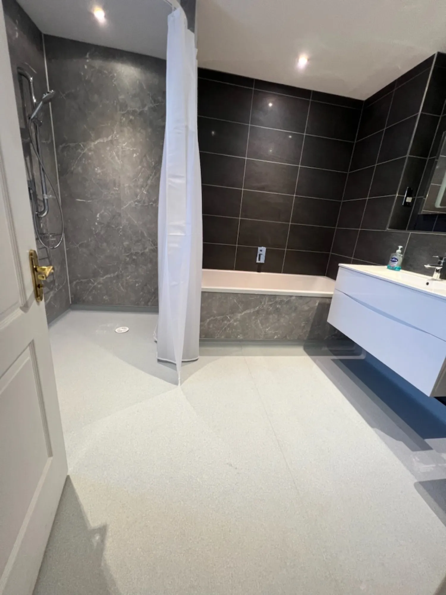 Bath with a glass screen against dark tiled walls