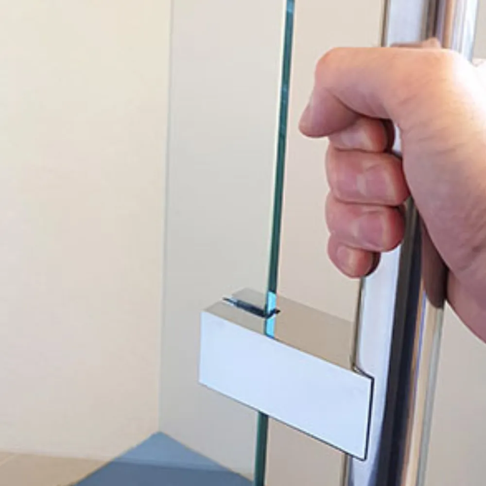 A hand holding the edge handle of a glass shower screen