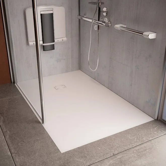 A low-profile white shower tray with a folding seat and support rails